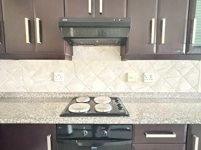 A functional kitchen featuring dark cabinetry, granite countertops, a built-in electric oven, hob, and extractor fan with a neutral tiled backsplash.