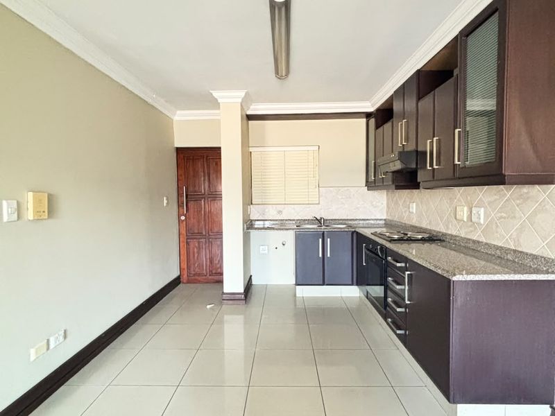 A functional kitchen featuring dark wood cabinetry, granite countertops, built-in appliances, and neutral tiled flooring in an open-plan layout.