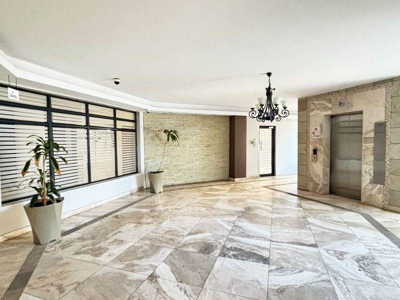 A spacious apartment building lobby featuring polished stone tile flooring, a stone feature wall, and a modern elevator access point.