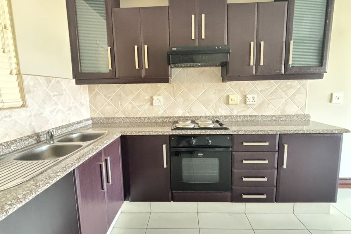 A functional kitchen featuring dark built-in cabinetry, granite countertops, a double sink, and integrated oven and hob with a tiled backsplash.