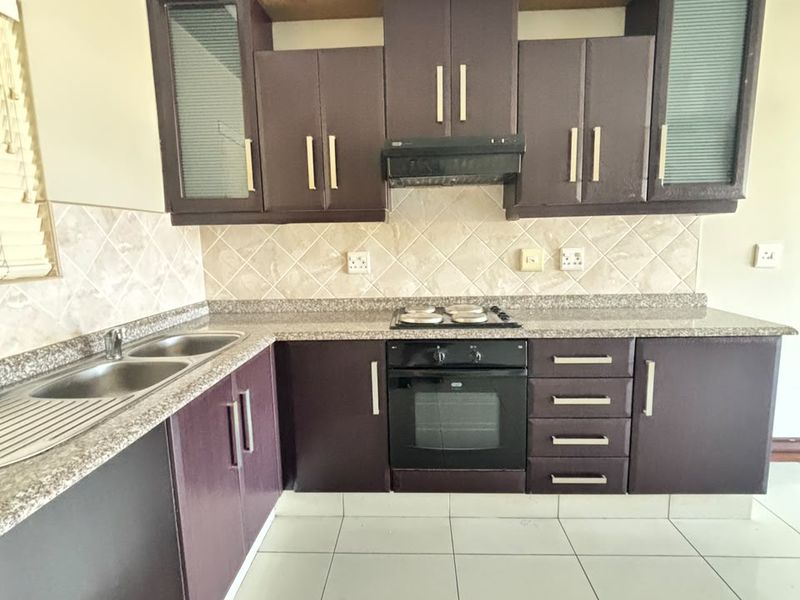 A functional kitchen featuring dark built-in cabinetry, granite countertops, a double sink, and integrated oven and hob with a tiled backsplash.