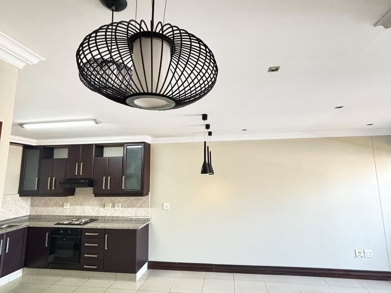 An open-plan living and kitchen area featuring dark cabinetry, granite countertops, built-in appliances, tiled flooring, and modern pendant lighting.