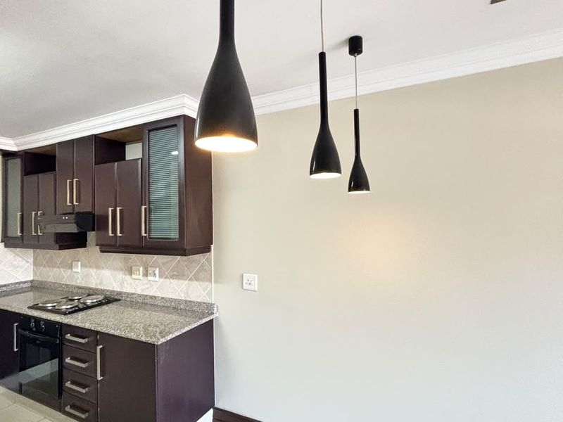 A modern kitchen featuring dark wood cabinetry, granite countertops, built-in oven and hob, tiled backsplash, and stylish pendant lighting.
