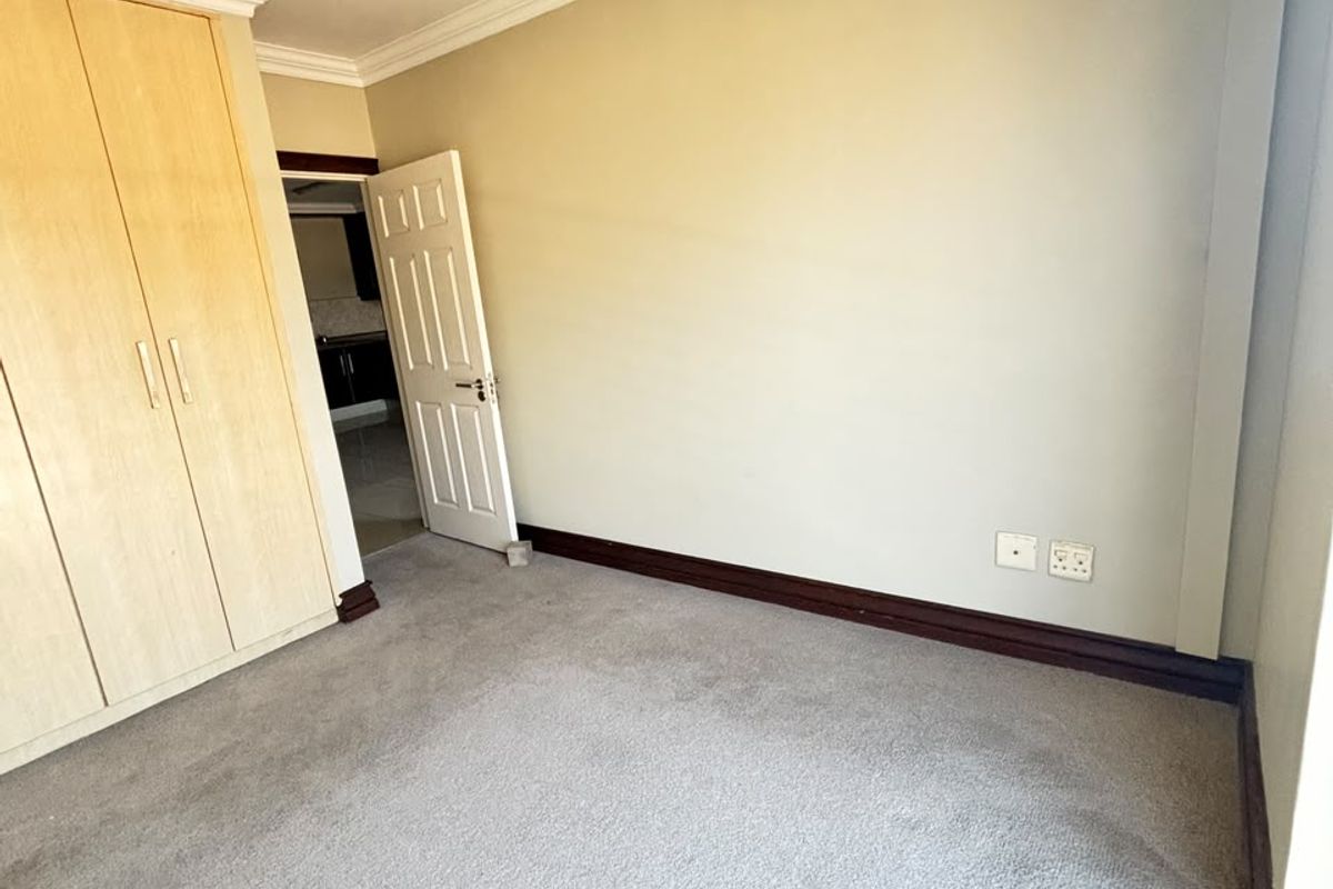 An empty bedroom featuring built-in cupboards, carpeted flooring, and a wall-mounted air conditioning unit.
