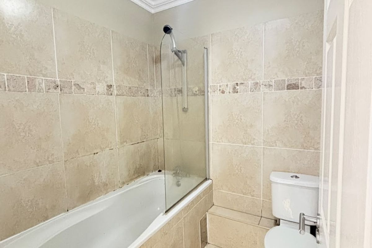 A functional bathroom featuring a bathtub with a glass shower screen, tiled walls, and a standard toilet.