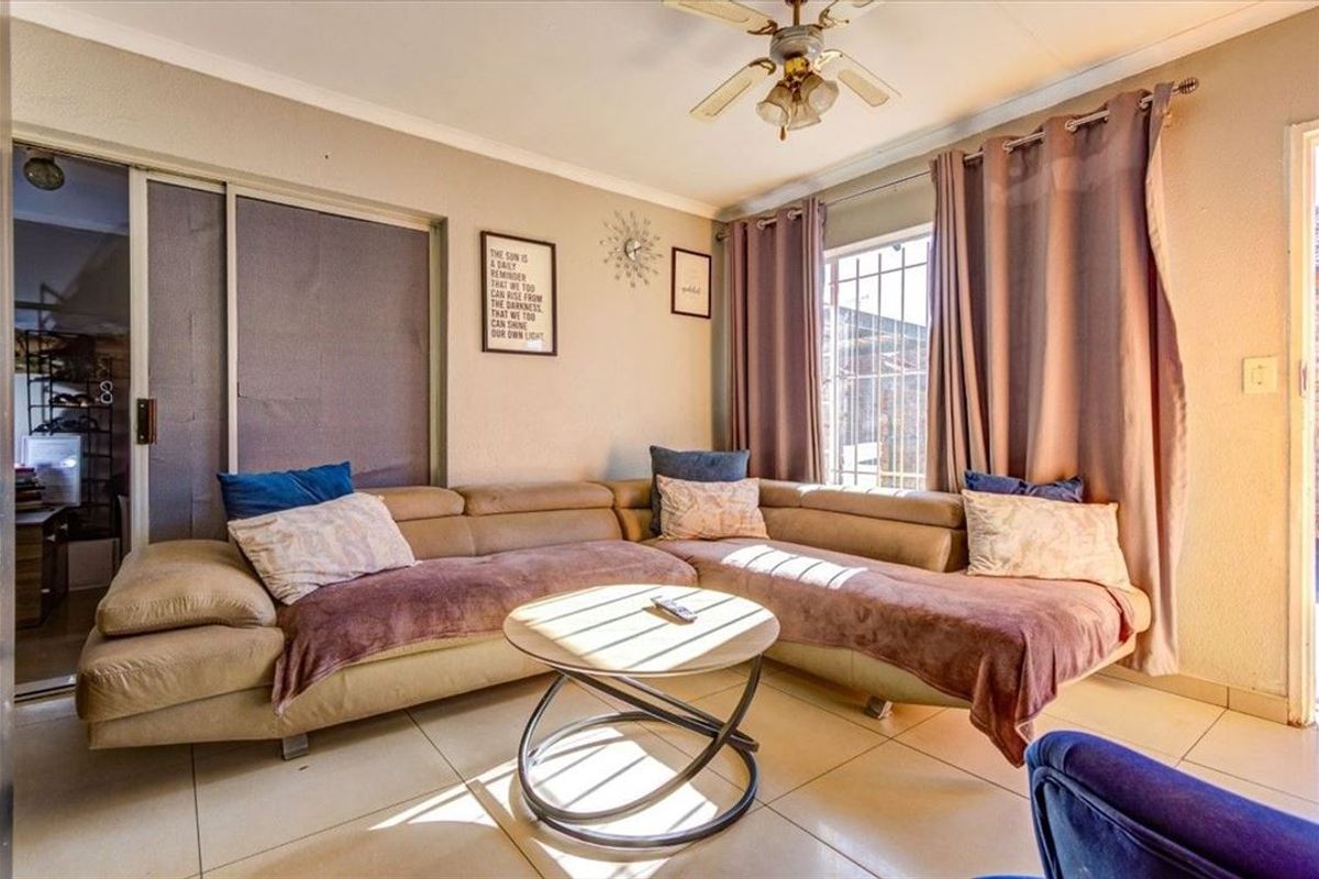 A comfortable living room featuring tiled flooring, a ceiling fan, and a sliding door with security bars, providing access to the exterior.