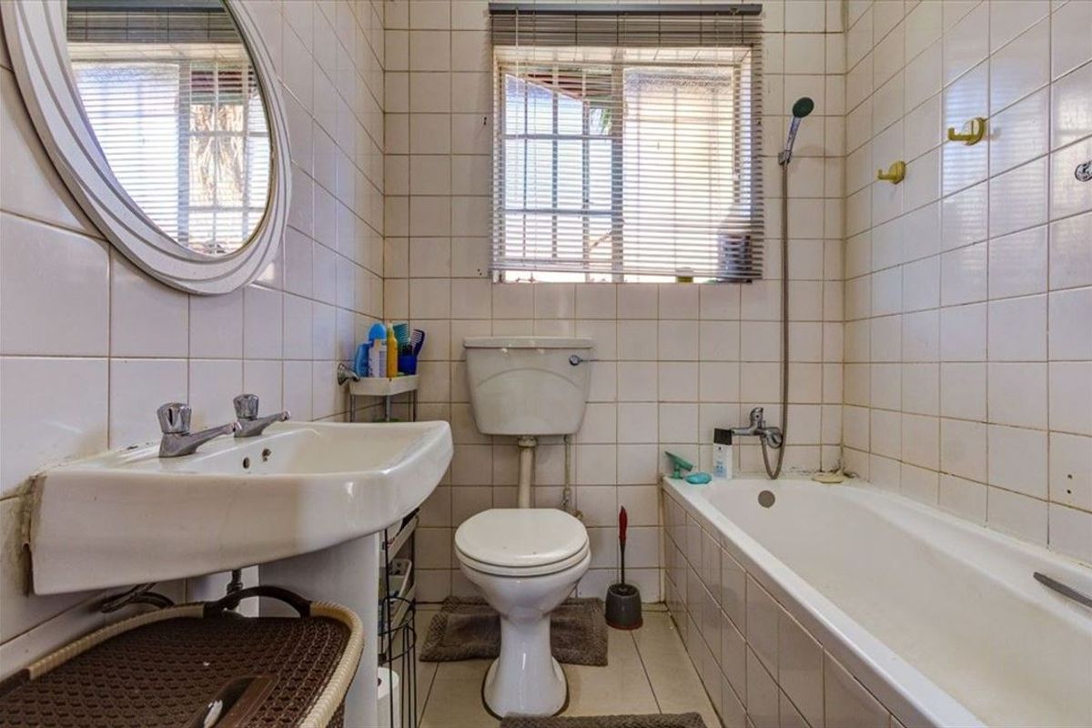 A functional bathroom featuring a pedestal basin, toilet, and bathtub with shower mixer, finished with full-height wall tiling and a window for natural light.