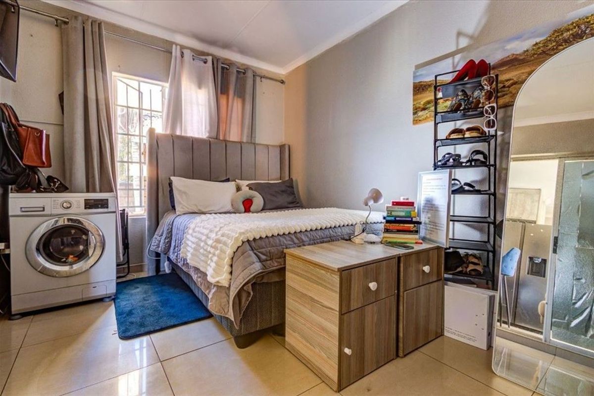A bedroom featuring tiled flooring and a window with security bars, currently utilized with a laundry appliance integrated into the living space.