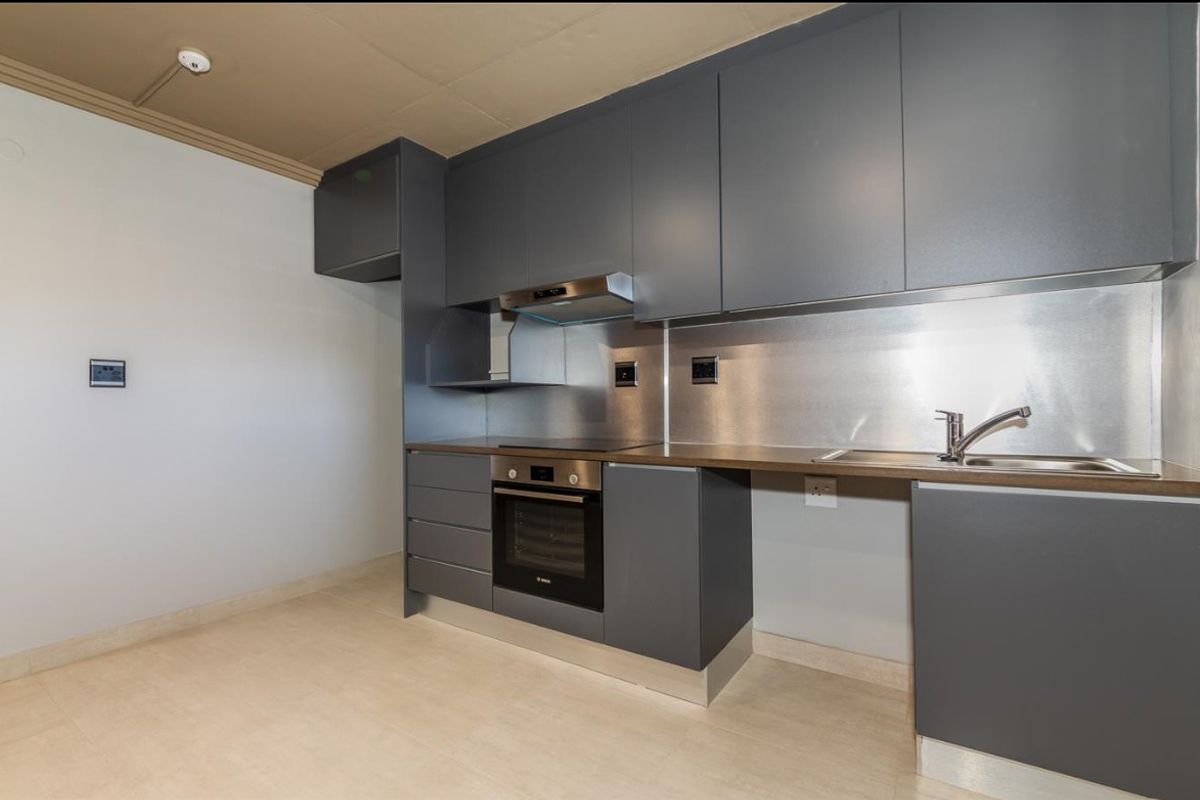 Modern kitchen featuring dark grey cabinetry, stainless steel splashback, integrated oven, hob, extractor fan, and a stainless steel sink with a mixer tap.