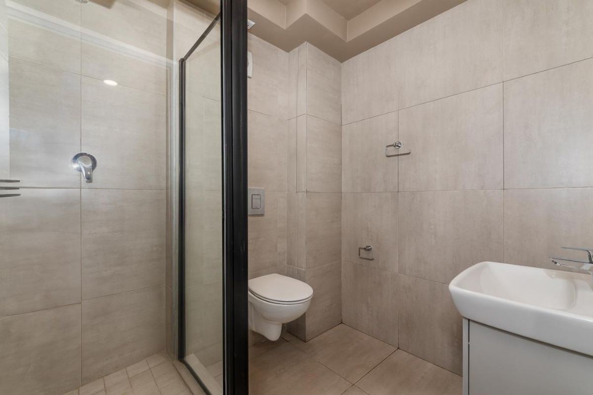 A modern, neutral-toned bathroom featuring a glass-enclosed shower, wall-mounted toilet, and a sleek vanity basin with chrome fixtures.