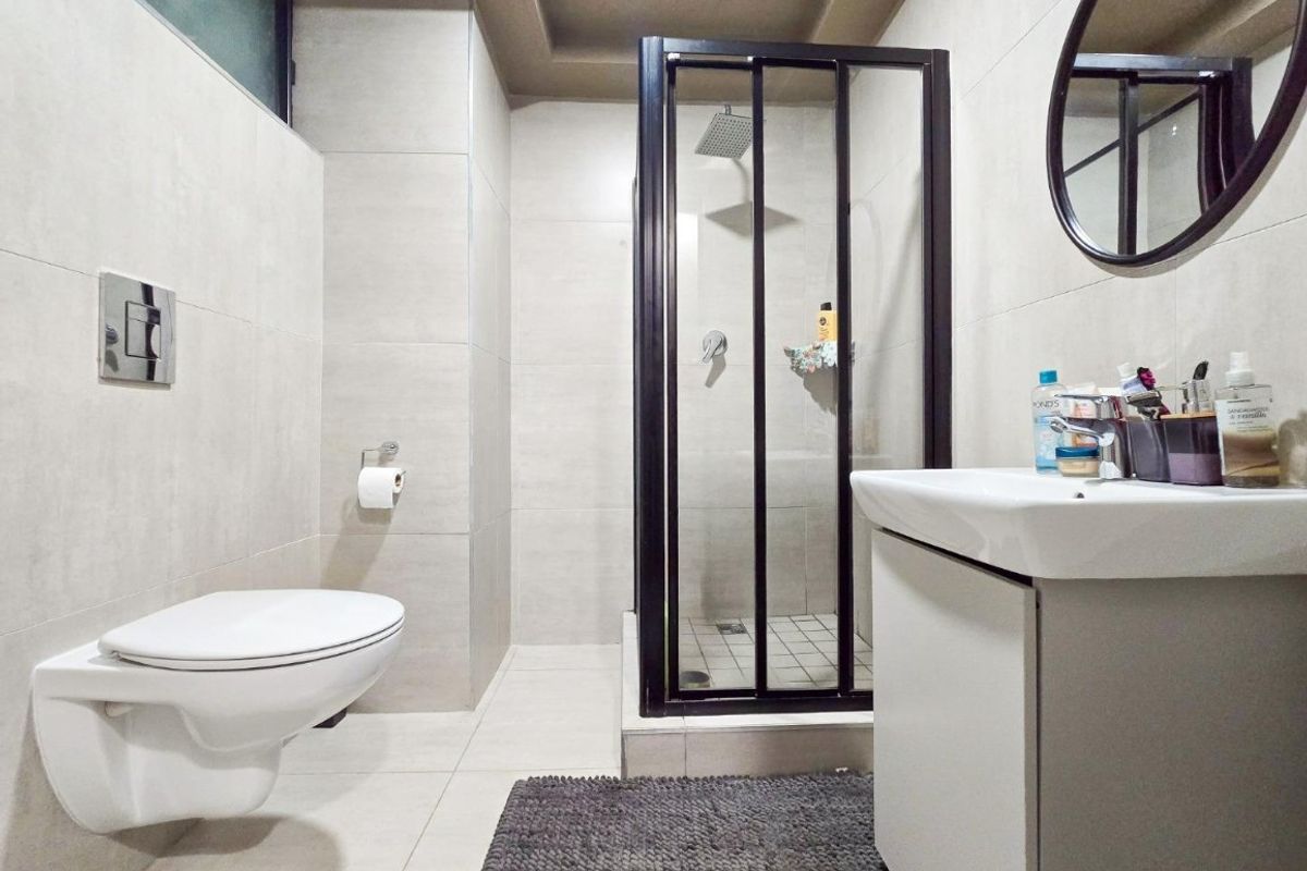 Modern bathroom featuring a wall-mounted toilet, a glass-enclosed shower, and a sleek vanity cabinet with a basin, finished with neutral wall and floor tiles.