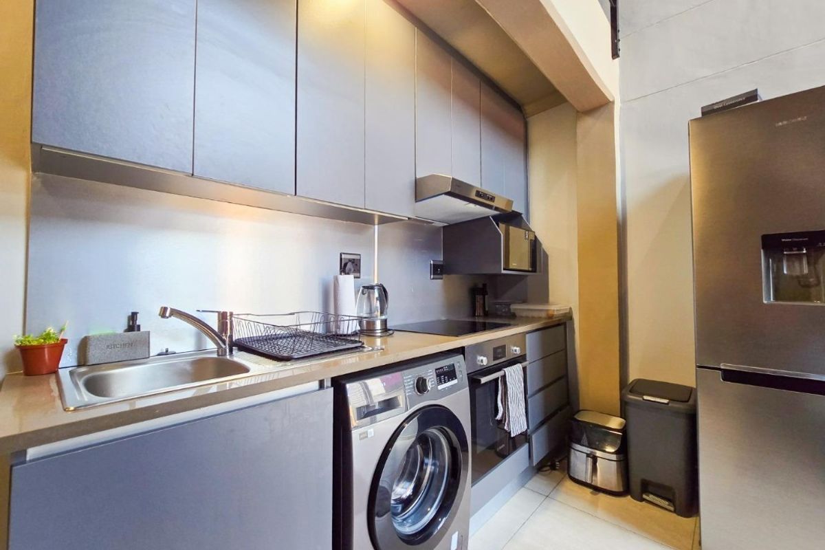Modern galley-style kitchen featuring sleek grey cabinetry, stainless steel appliances, integrated washing machine, and durable tiled flooring.