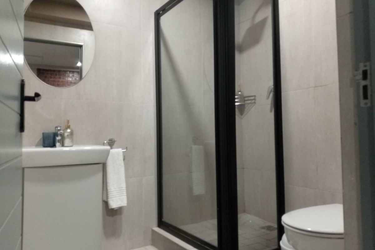 A modern bathroom featuring a glass-enclosed shower, a sleek vanity basin, and a wall-mounted mirror with neutral tiling throughout.