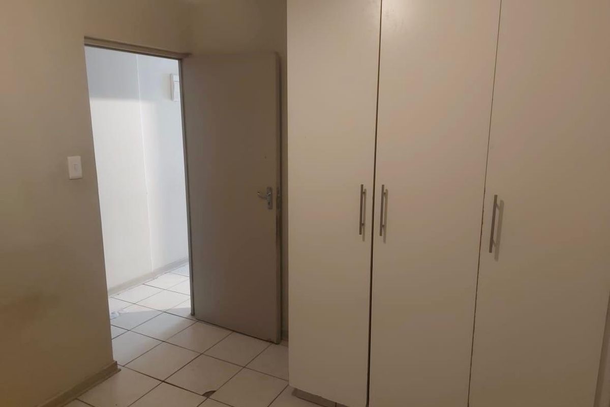 A simple bedroom featuring built-in cupboards and tiled flooring, offering a clean and functional space ready for personalization.