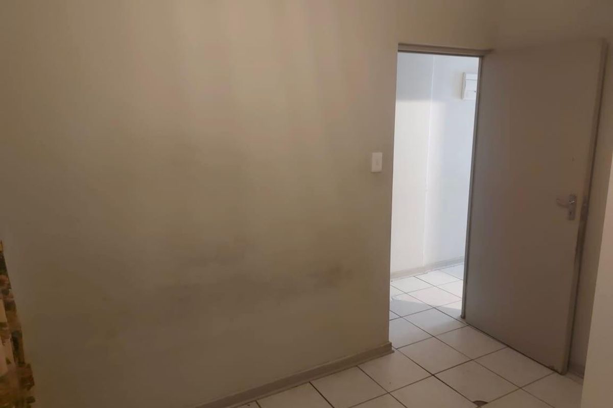An empty bedroom featuring tiled flooring and a standard internal door, showing visible signs of wall wear and staining.