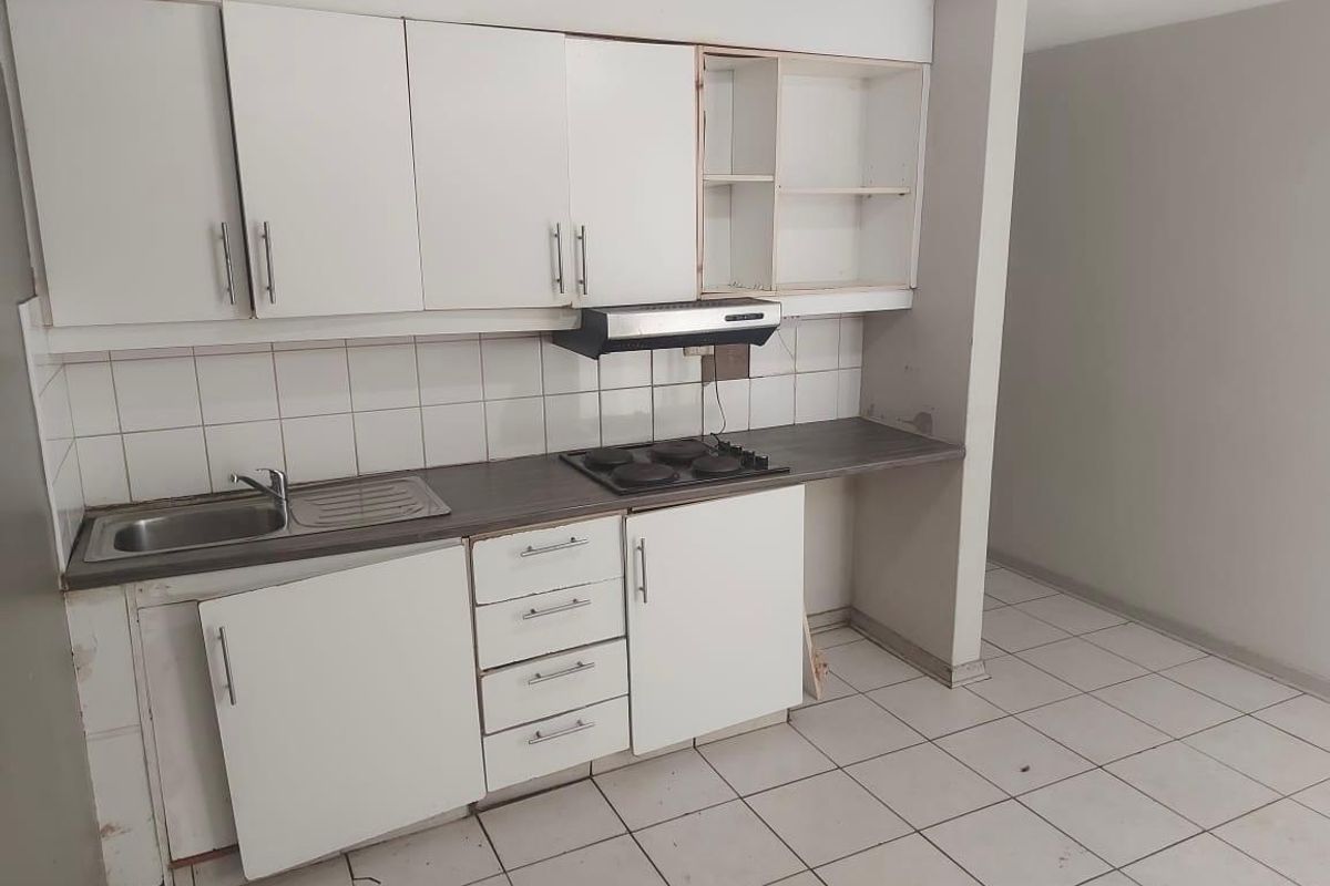 A dated kitchen featuring white cabinetry, a stainless steel sink, and an electric hob, currently in need of repairs and cosmetic updates.