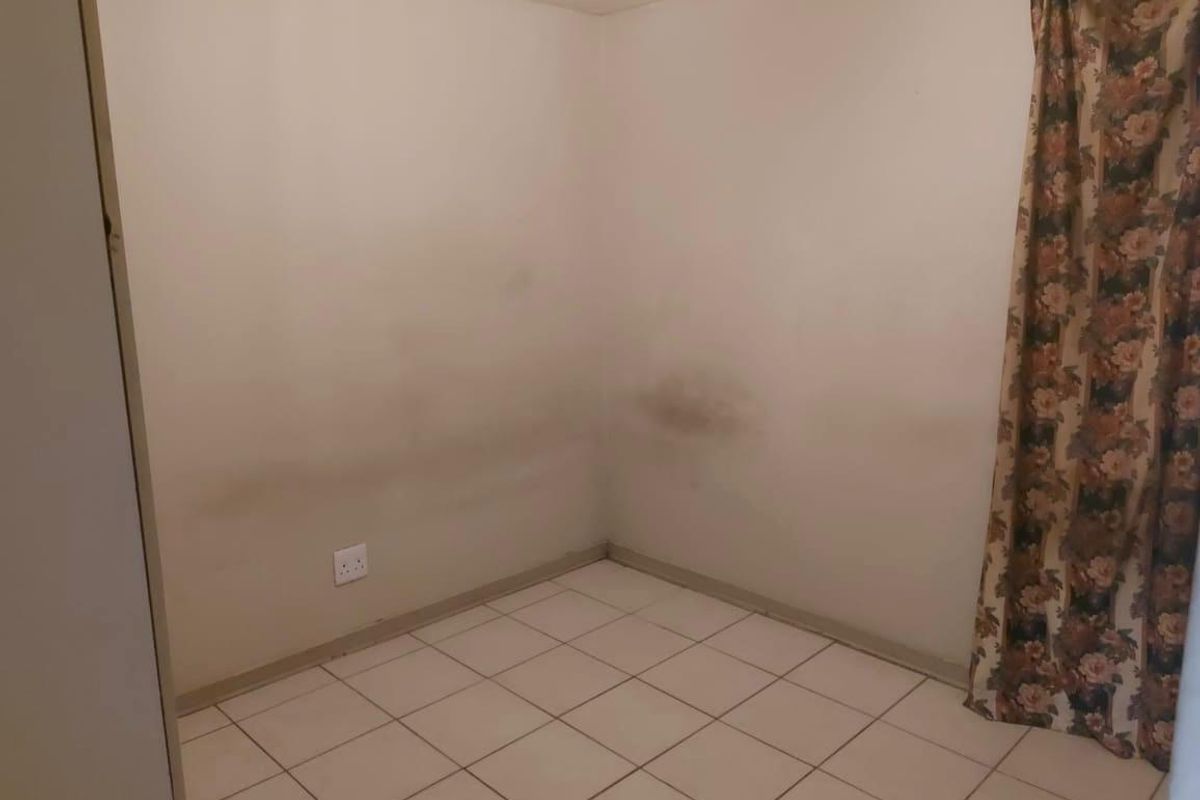 An empty bedroom featuring tiled flooring and walls showing signs of staining and discoloration, requiring cosmetic attention.