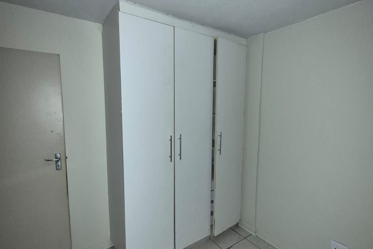 A vacant bedroom featuring tiled flooring and a built-in wardrobe, requiring minor cosmetic updates and fixture repairs.