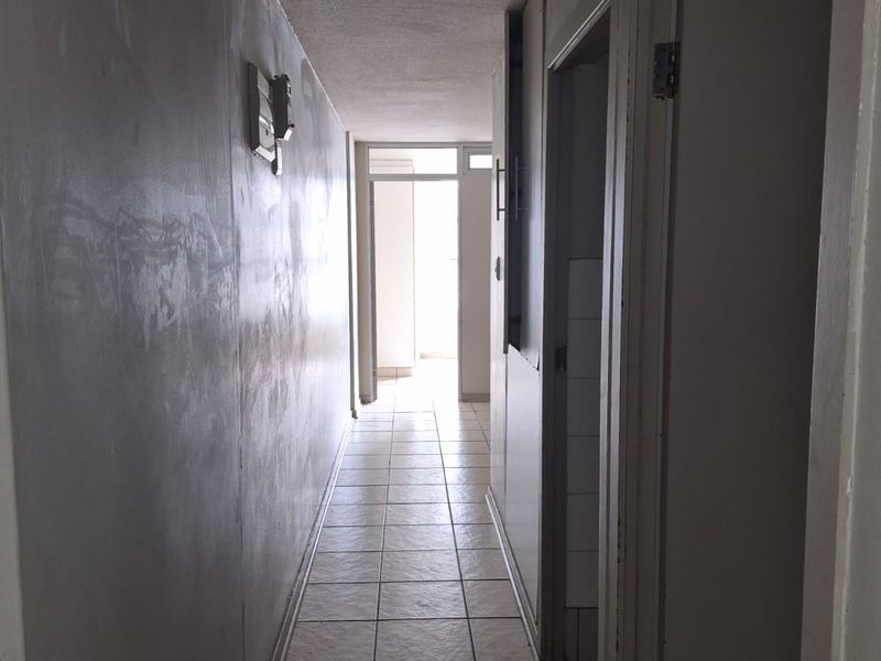 A narrow hallway featuring tiled flooring and unfinished wall surfaces, providing access to adjacent rooms within the apartment.