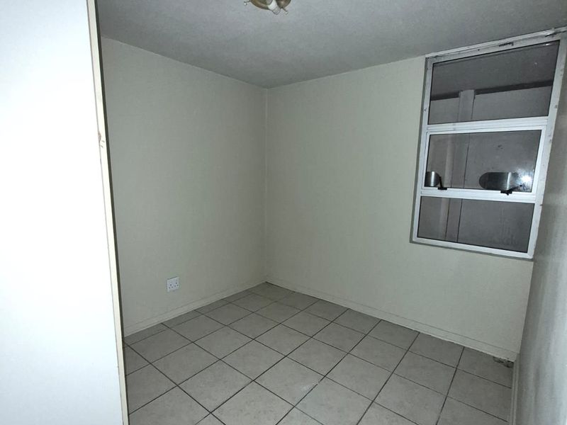 An empty bedroom featuring tiled flooring and an aluminium window frame, presenting a blank canvas for potential renovation or interior design updates.