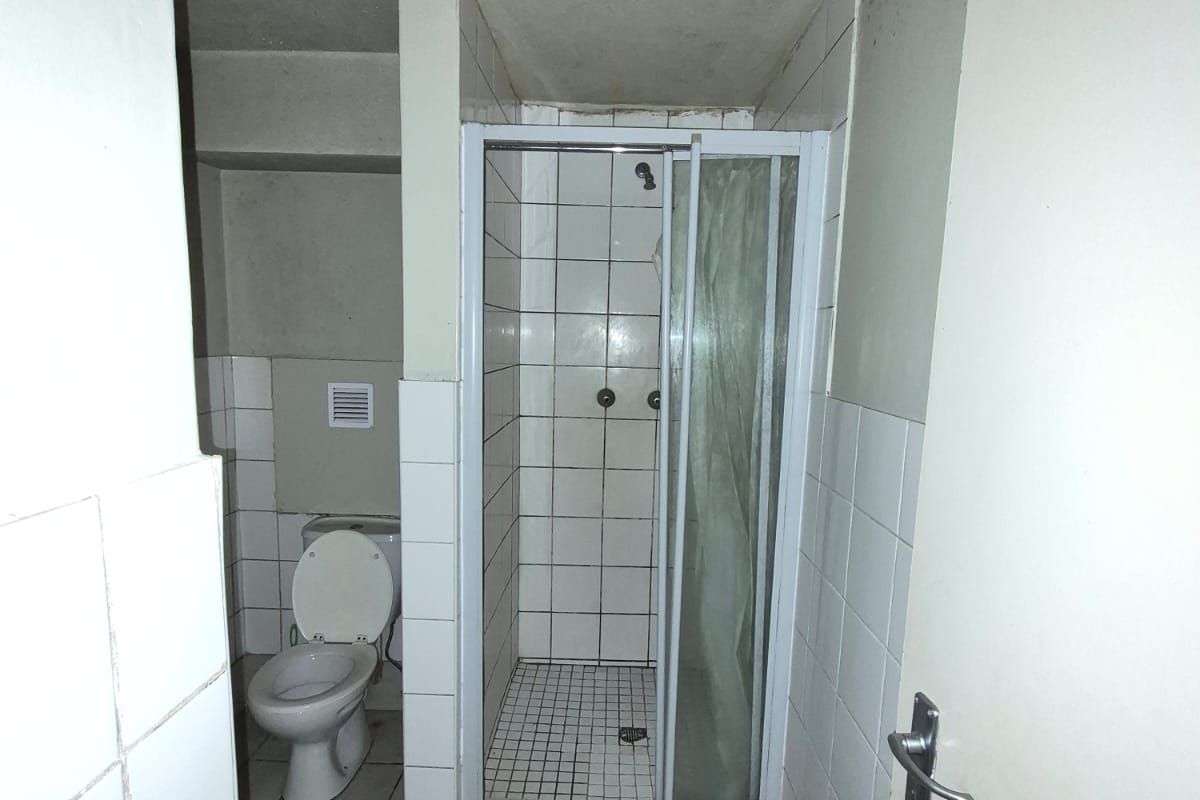 A dated bathroom featuring a shower enclosure and toilet, showing significant signs of wear and staining on the walls and ceiling.