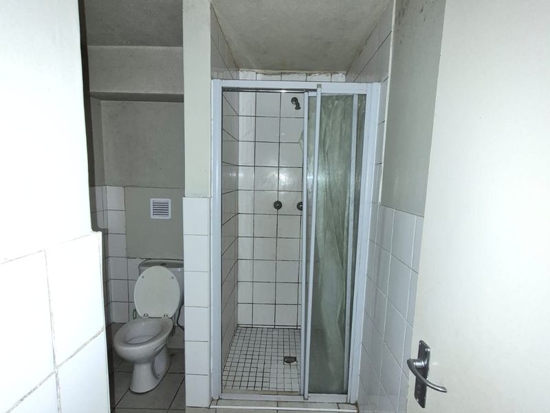 A dated bathroom featuring a shower enclosure and toilet, showing significant signs of wear and staining on the walls and ceiling.