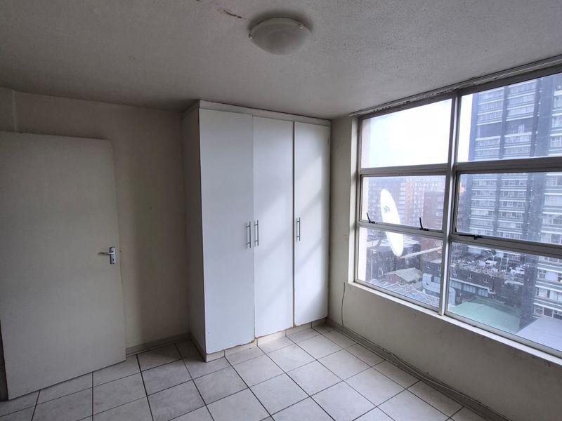 A vacant bedroom featuring tiled flooring, a built-in wardrobe, and large windows offering an urban view.