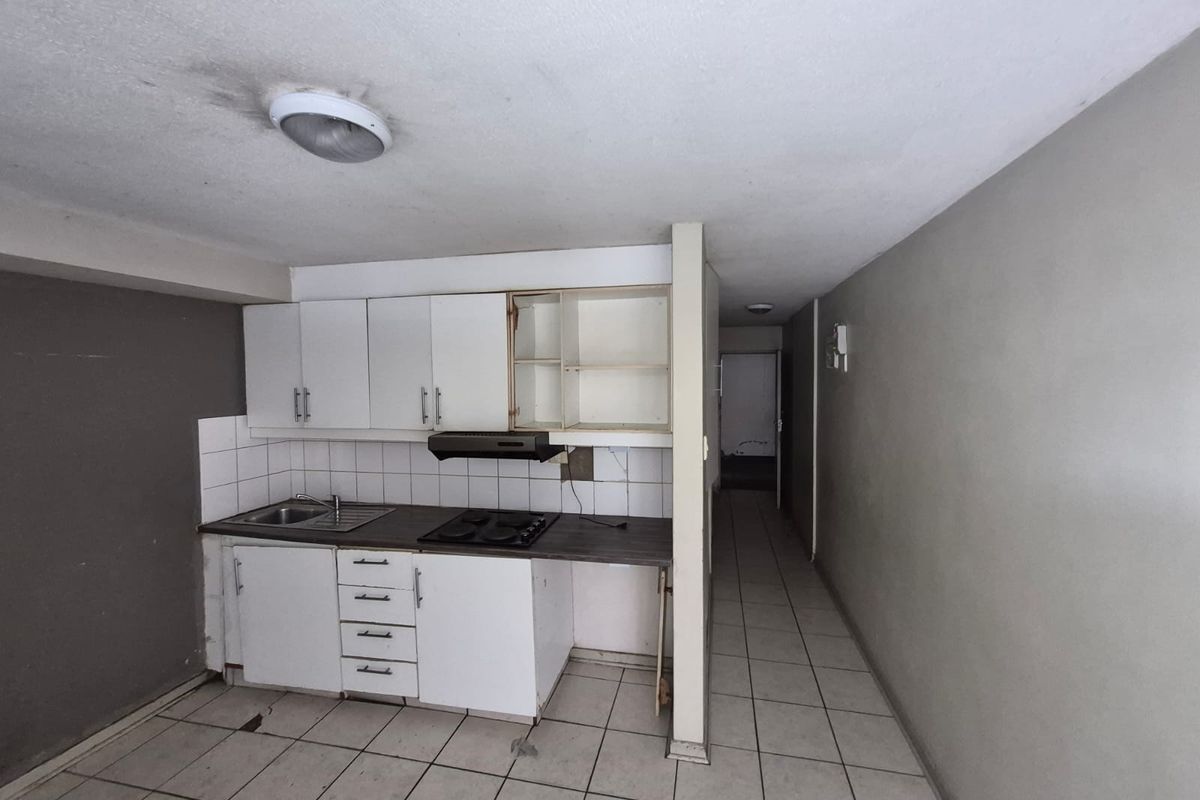 A compact kitchen area featuring built-in cabinetry, a hob, and extractor fan, requiring cosmetic updates and repairs to finishes.