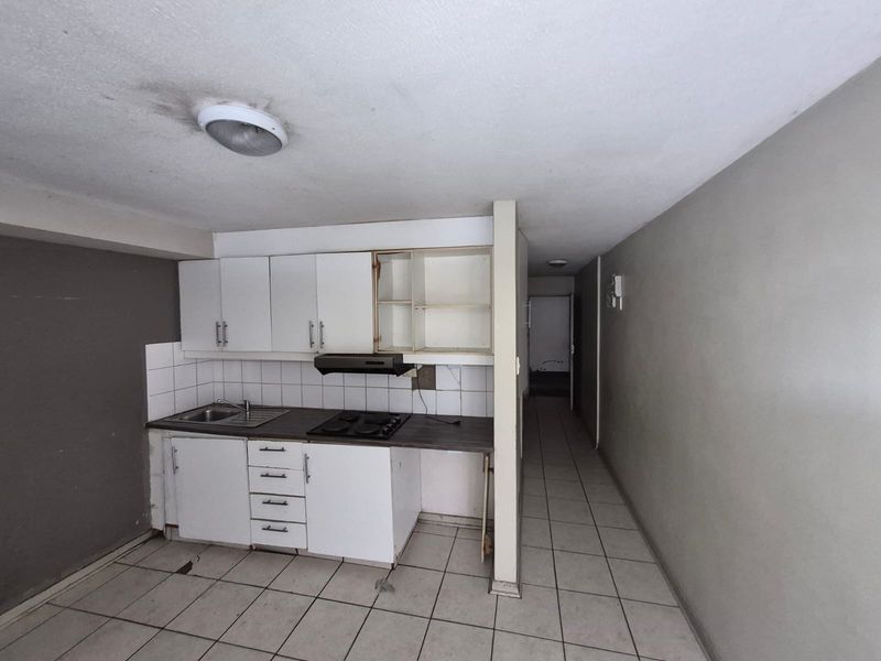 A compact kitchen area featuring built-in cabinetry, a hob, and extractor fan, requiring cosmetic updates and repairs to finishes.