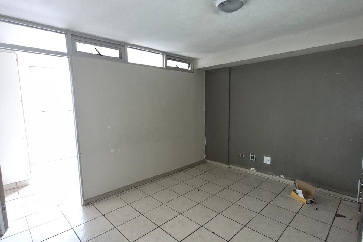 An empty living area featuring tiled flooring, neutral wall finishes, and natural light access through an adjacent doorway.