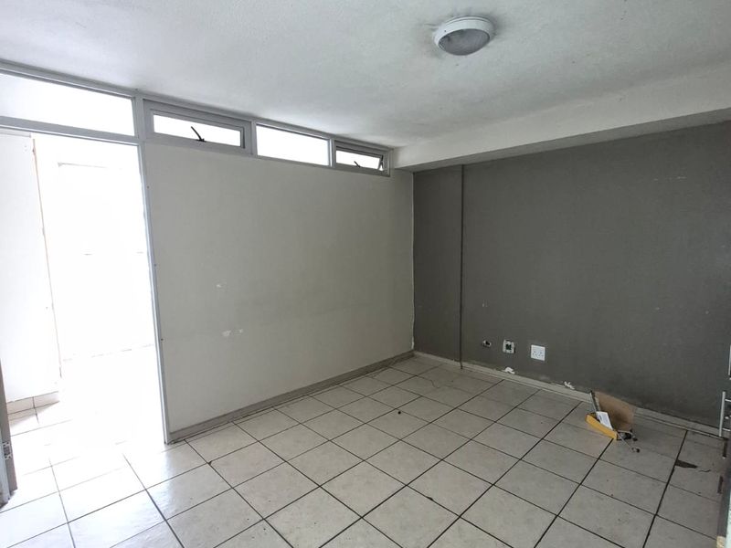 An empty living area featuring tiled flooring, neutral wall finishes, and natural light access through an adjacent doorway.