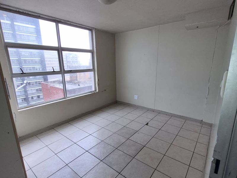 An empty bedroom featuring tiled flooring and a large window with urban views, requiring cosmetic updates to the ceiling and flooring.