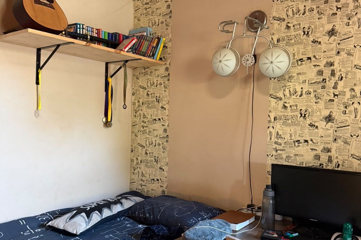 A bedroom featuring a timber ceiling and decorative wallpaper, currently used as a study and sleeping area.
