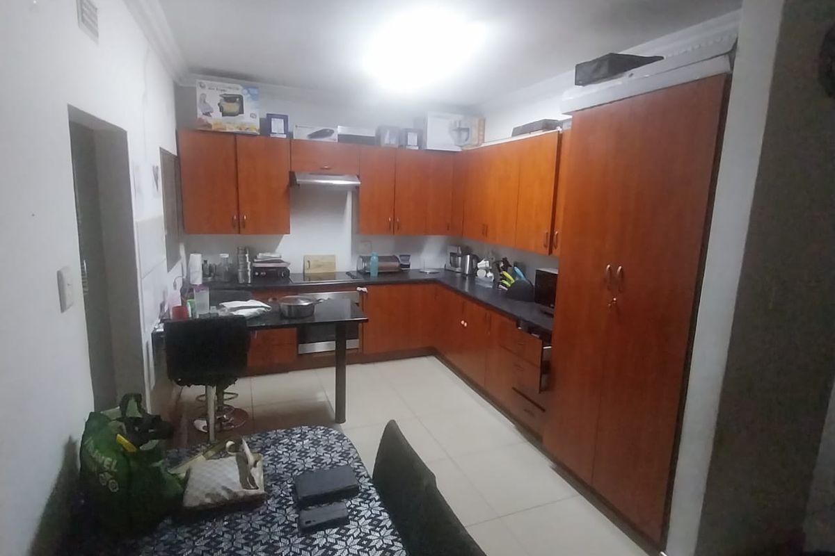 A functional kitchen featuring wood-tone cabinetry, dark countertops, built-in oven, and extractor fan, with tiled flooring and decorative ceiling coving.