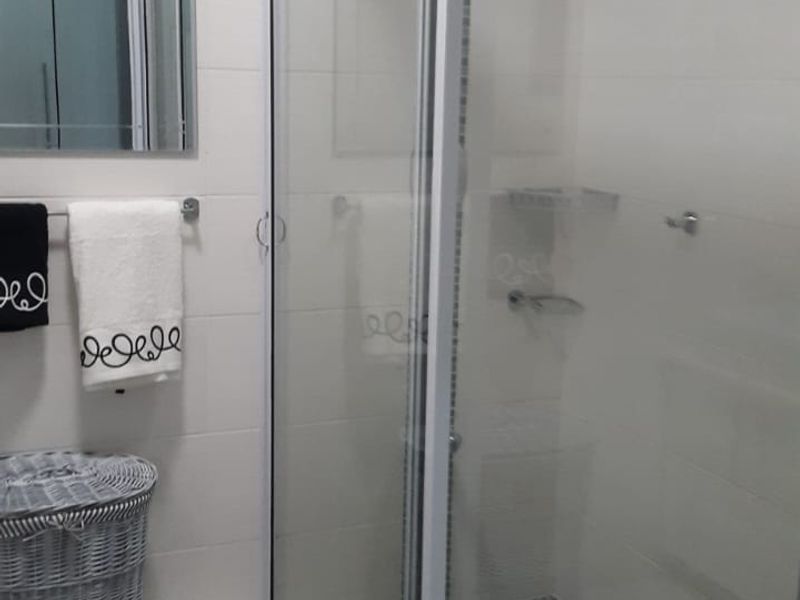 A clean, modern bathroom featuring a walk-in shower with a sliding glass door, tiled flooring, and a wall-mounted mirror.