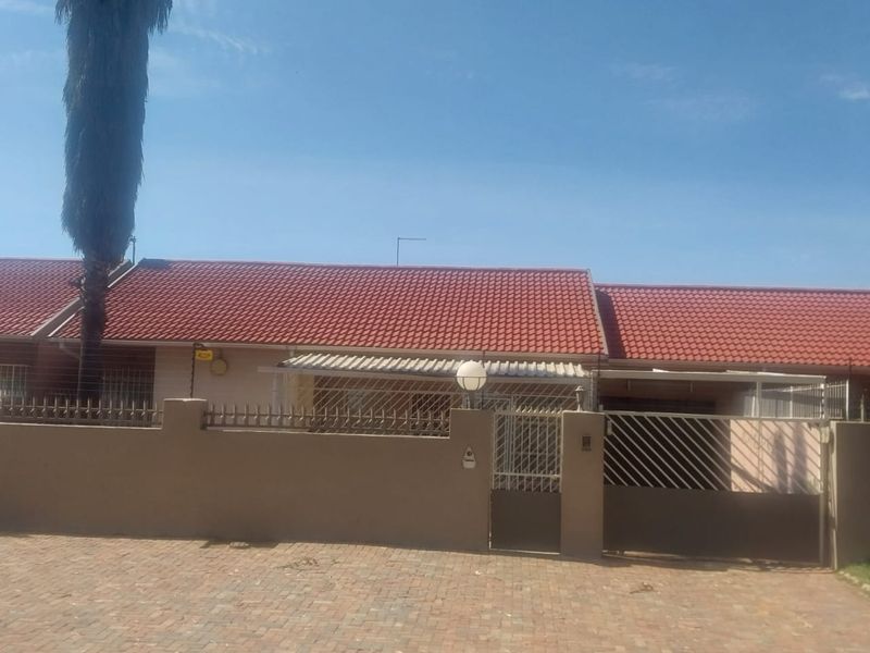 Front elevation of a single-story house featuring a tiled roof, paved driveway, and secure perimeter wall with gated access.
