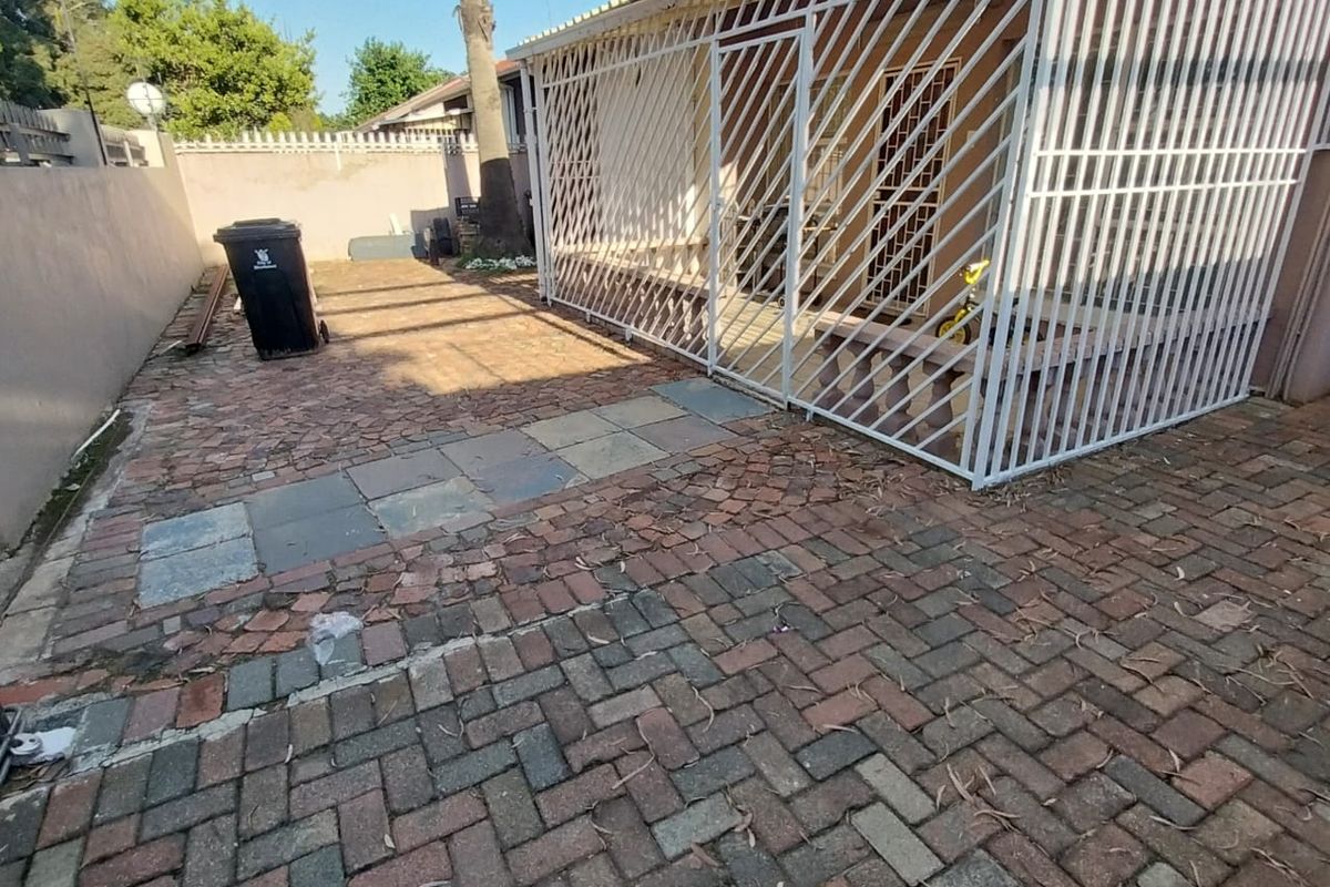 Rear exterior area featuring a paved patio and a covered section enclosed by security gates, bordered by a perimeter wall.