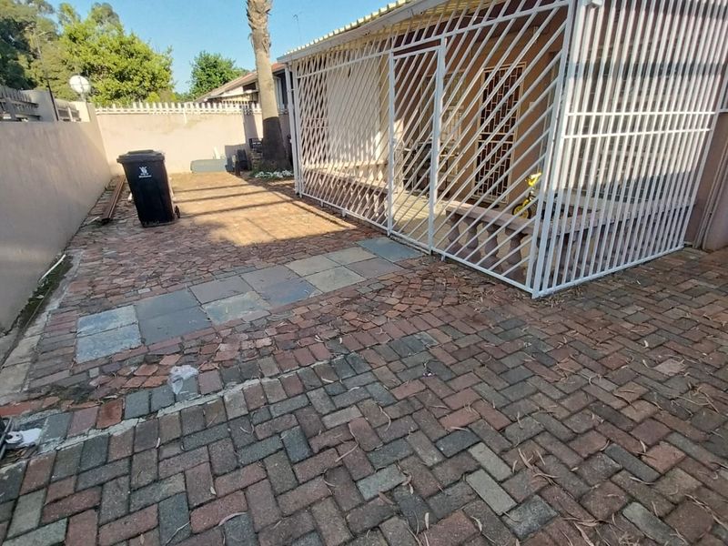 Rear exterior area featuring a paved patio and a covered section enclosed by security gates, bordered by a perimeter wall.