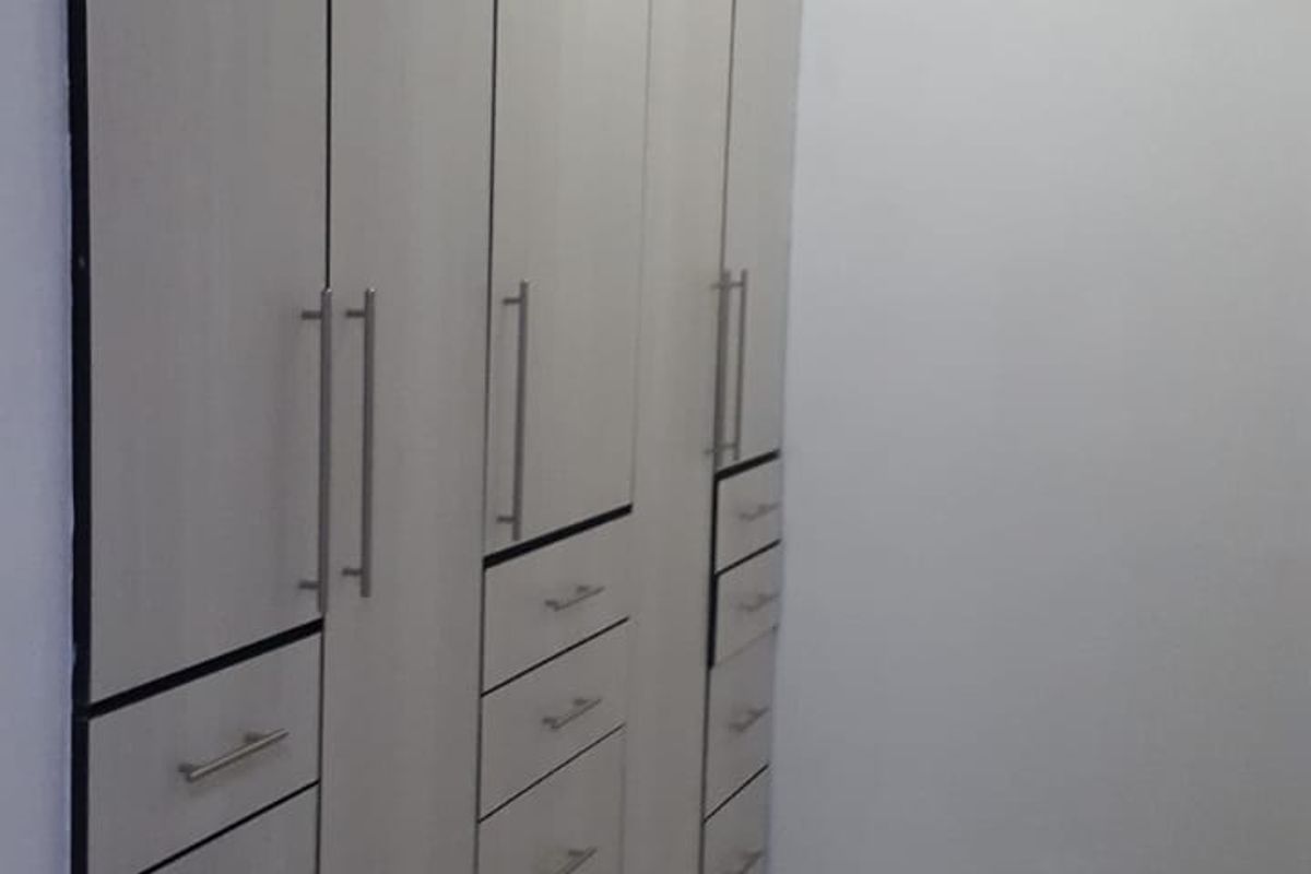 A clean, empty bedroom space featuring extensive floor-to-ceiling built-in cupboards with modern handles and neutral tiled flooring.