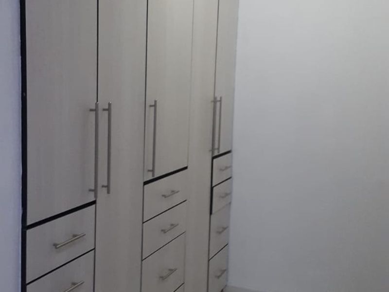 A clean, empty bedroom space featuring extensive floor-to-ceiling built-in cupboards with modern handles and neutral tiled flooring.