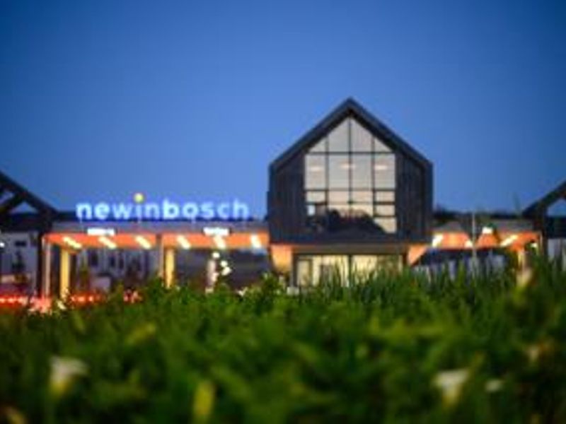 Modern architectural entrance facade of the Newinbosch development, featuring a striking gabled design with extensive glass elements and integrated evening lighting.