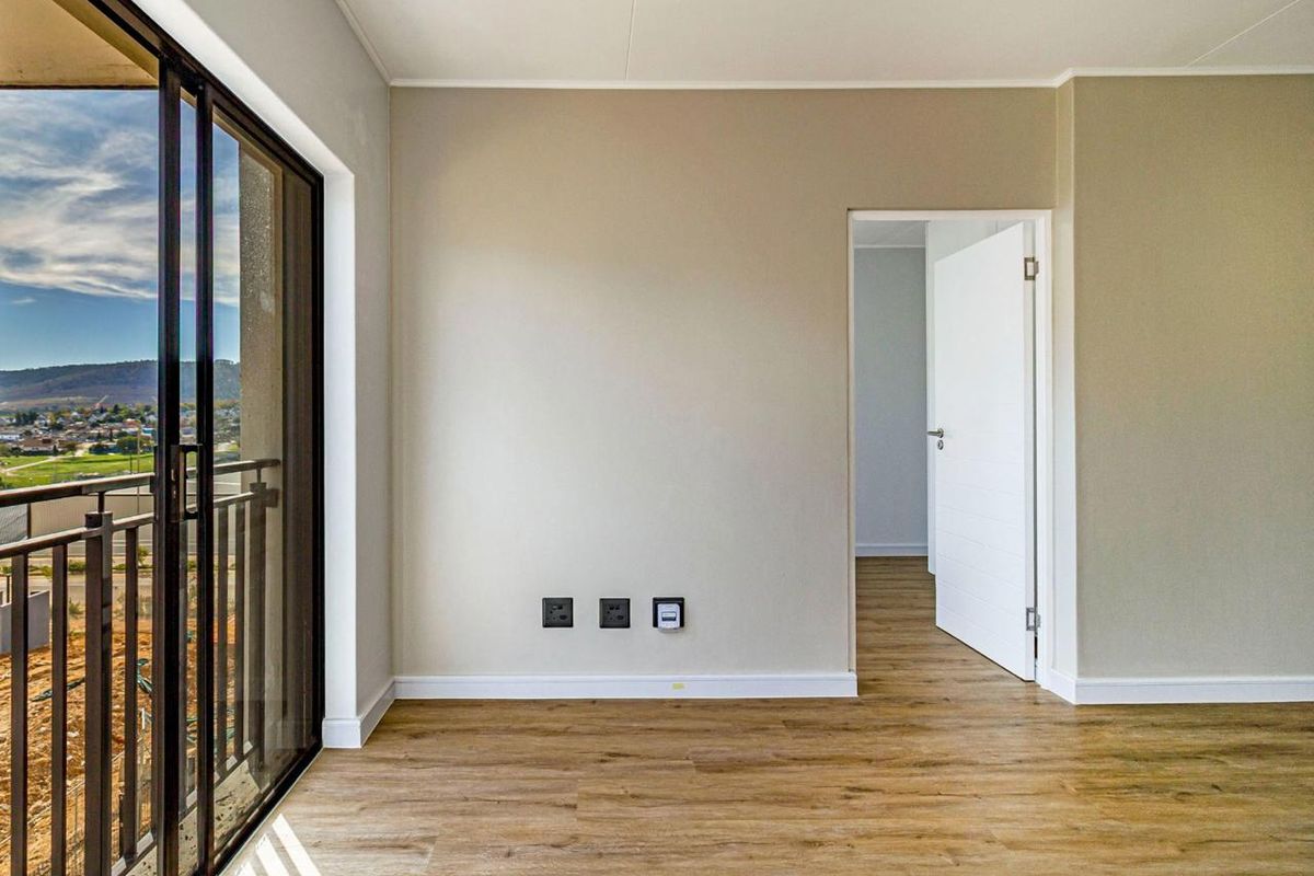 A bright, empty living room featuring modern laminate flooring, neutral walls, and a sliding glass door providing access to a balcony with scenic views.