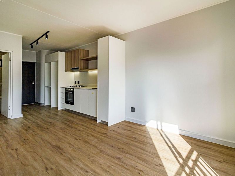 Modern open-plan living area featuring a sleek kitchen with built-in appliances, laminate flooring, and neutral finishes throughout.