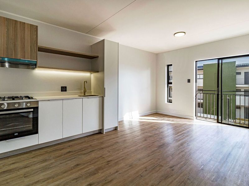 Modern open-plan kitchen and living area featuring sleek cabinetry, built-in appliances, laminate flooring, and direct access to a private balcony.