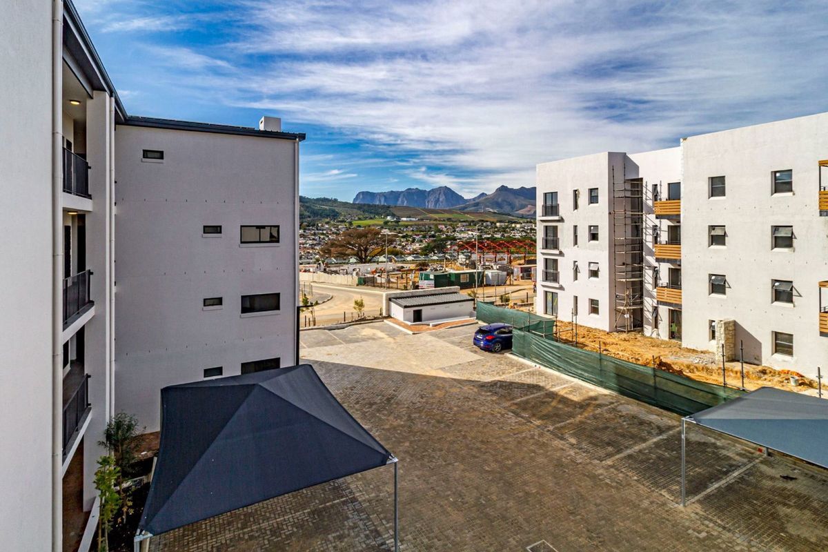 Aerial view of a modern apartment complex featuring paved parking areas with shade sails and surrounding mountain views.