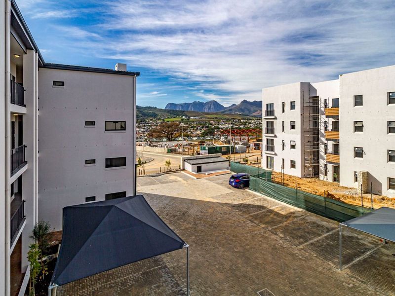 Aerial view of a modern apartment complex featuring paved parking areas with shade sails and surrounding mountain views.