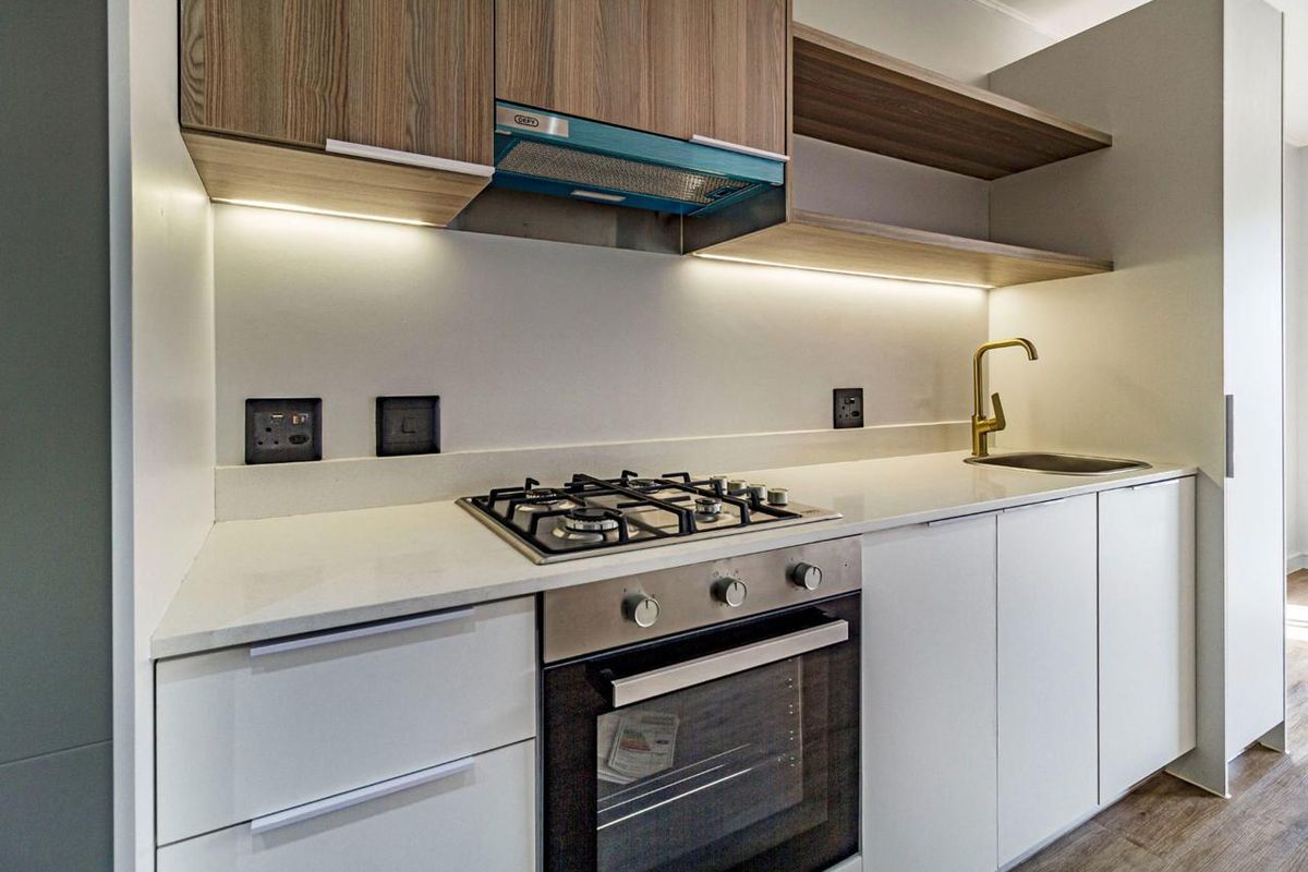 Modern kitchen featuring a gas hob, built-in oven, extractor fan, stone countertops, brass faucet, and sleek cabinetry with integrated under-cabinet lighting.