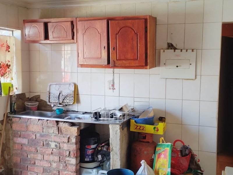 A dated kitchen area featuring a brick-based sink unit, wall-mounted wooden cabinetry, and tiled splashbacks, requiring renovation to modernize the space.