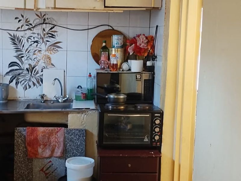 A compact kitchen area featuring dated cabinetry, tiled splashbacks, and tiled flooring, requiring modernization to improve functionality and aesthetic appeal.