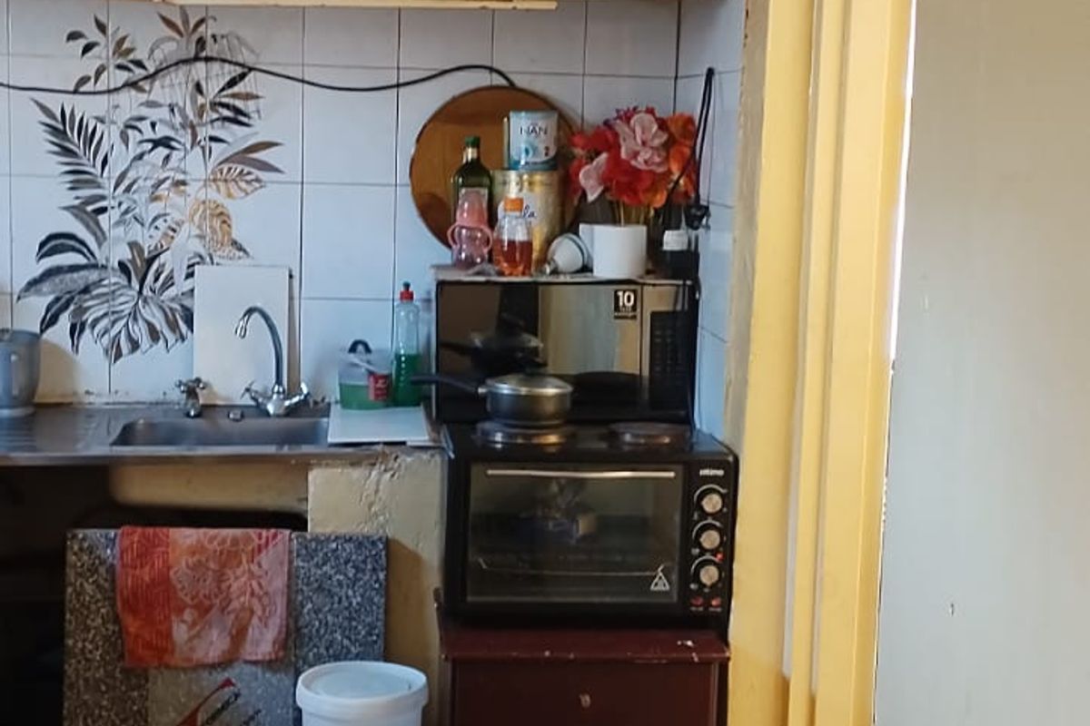 A compact kitchen area featuring dated cabinetry, tiled splashbacks, and tiled flooring, requiring modernization to improve functionality and aesthetic appeal.